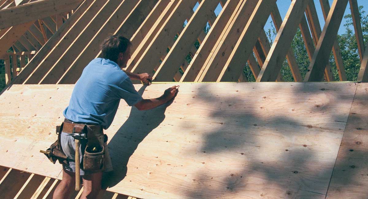 The sheathing straightens the rafters. Before nailing off the sheathing, a tape is hooked to the rafter on one end, and the rafter layout is marked along one edge. The rafters are then moved to the mark and nailed in place.