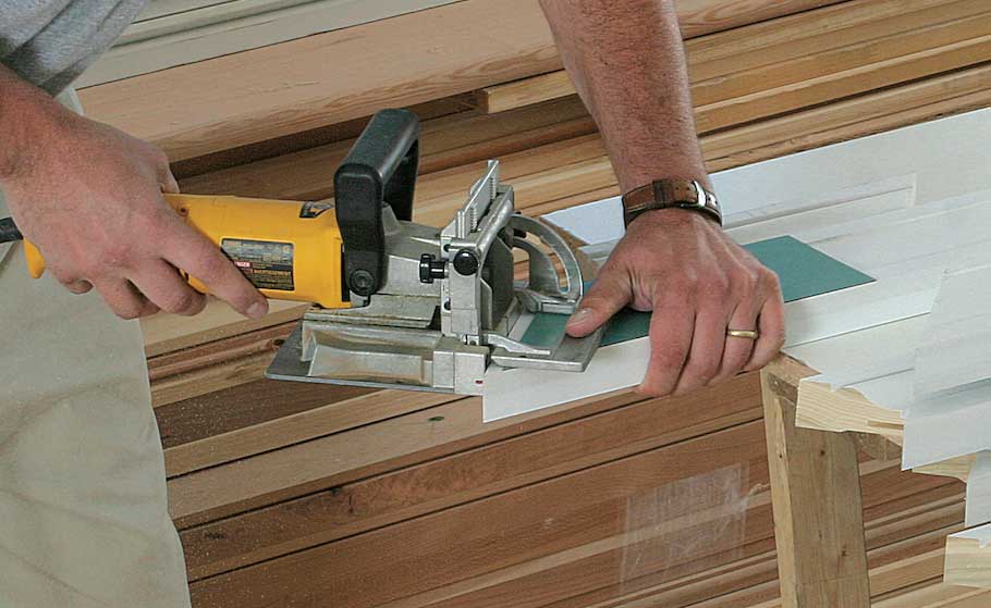 Slot all the miters at once to save time. After the stock has been cut to a rough length and mitered, the mitered ends are slotted for biscuits. To speed the process, each piece is partially pulled from the pile and slotted from the back; the miter’s short point is used as the biscuit joiner’s reference point.