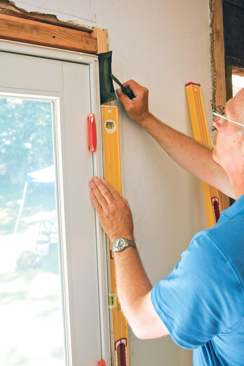 With the help of a 6-ft. level, the ­author matches the door to the wall’s out-of-plumb condition as best he can without sacrificing the door’s operation.
