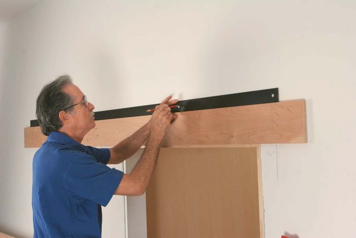 Mark the holes. A scrap-plywood ledger holds the track while the screw holes are transferred to the wall.