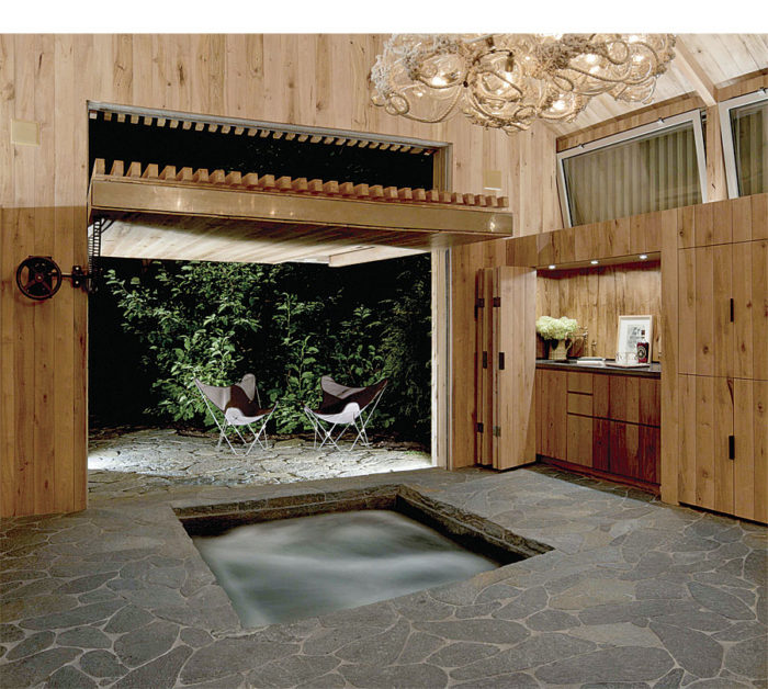 A 10-ft. by 10-ft. counterbalance door lifts up and outward to connect the interior and exterior. The millwork is reclaimed chestnut, and the flooring is galaxy schist from a local quarry. The water in the hot tub is treated with natural enzymes, allowing it to be collected along with rainwater in a cistern and then used to water the lawn and gardens.