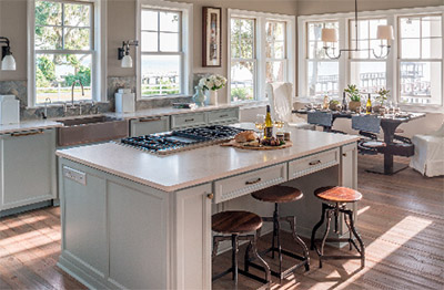 An open concept together with a neutral color palette reflect the serene natural setting highlighted through the kitchen’s wall of windows. Open concept design and airy features make this kitchen ideal for both entertaining and easy island living.
