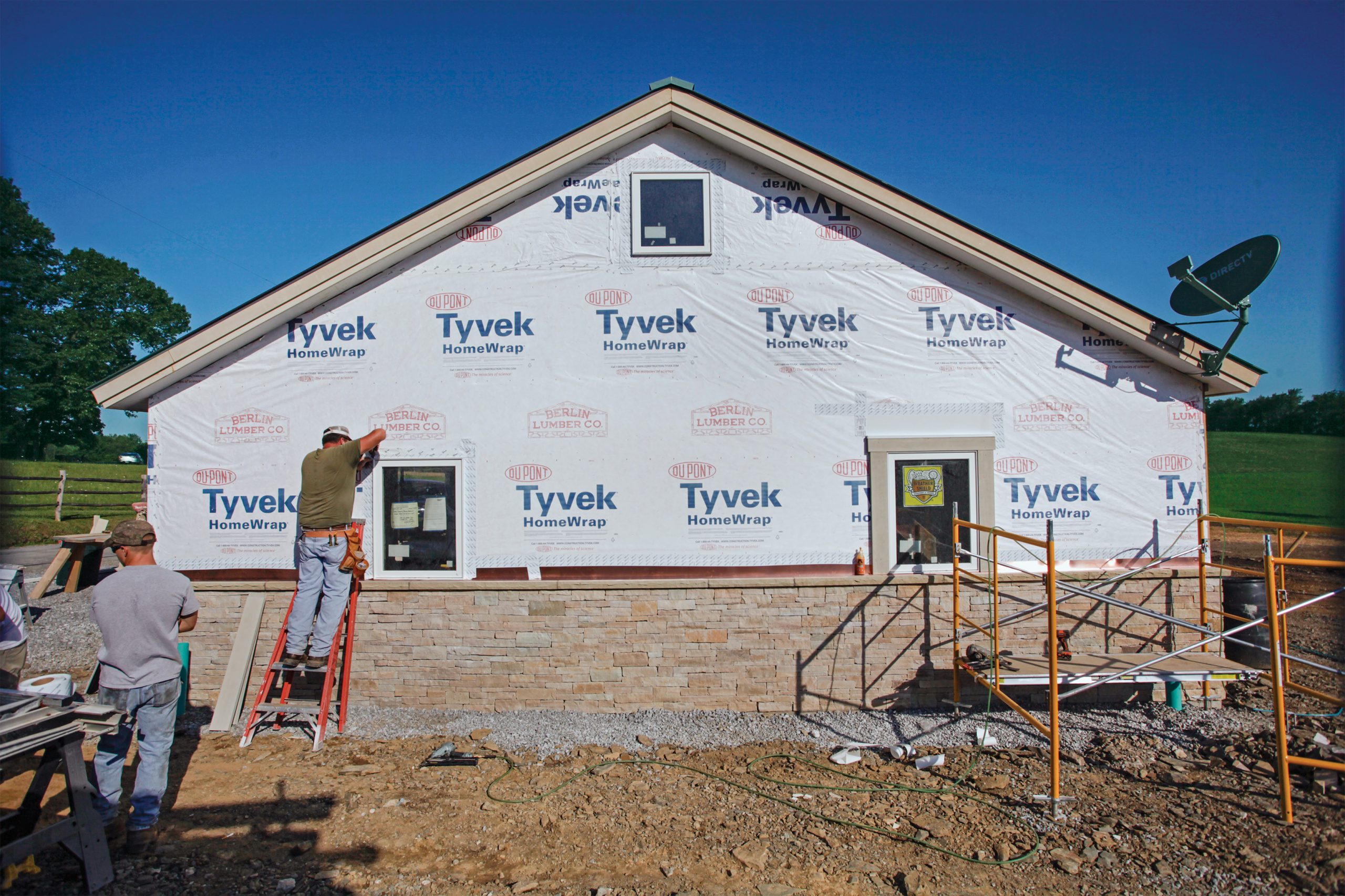 a man on a ladder, prepping the exterior wall for siding