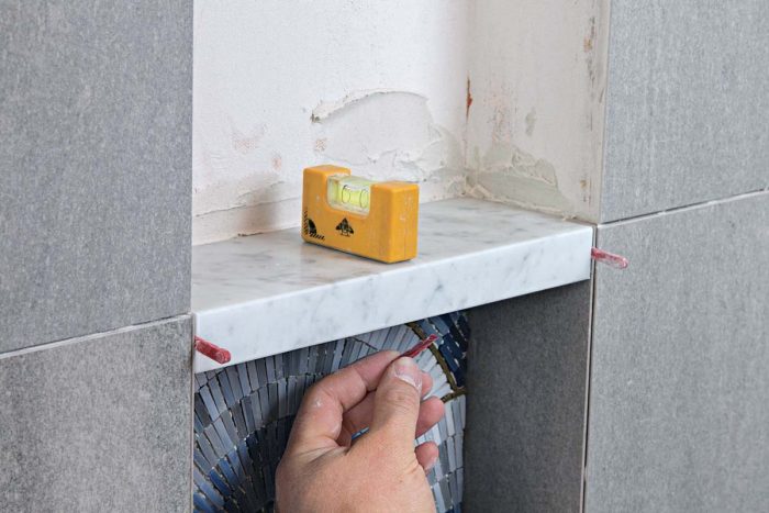 The shelf needs the same subtle downward slope as the bottom of the niche, and wedge spacers ensure thin, even grout lines at the side and bottom edges.