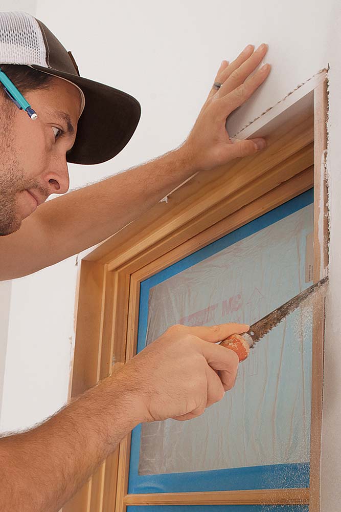 Using a wallboard saw to cut back drywall around a window