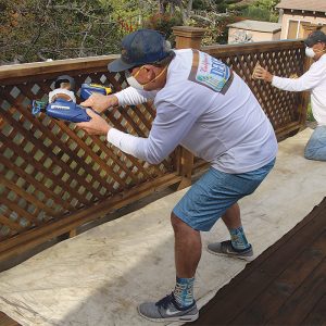 Start at the top. Vertical surfaces and anything above the deck get coated before moving to the deck surface. A small airless sprayer is great for coating railings, but once the coating is sprayed, work it into the surface and absorb any excess with a painting pad.