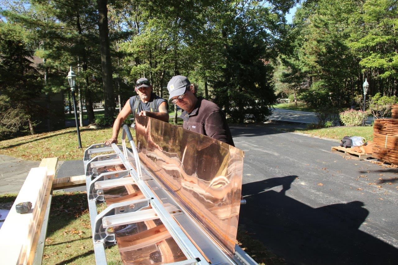 Two people work on bending a large sheet of copper