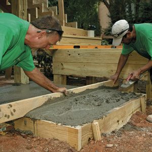 A level form is critical. A concrete pad is formed to terminate the two-tread run from the landing above. After setting and filling the form, screed the concrete flush with the top of the form, and trowel it smooth.