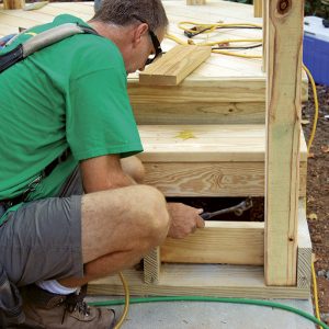 Frame the stairs. Once the pad has cured, the stairs from the landing can be built. Attach the short stringers to a 2x nailer bolted to the pad. Blocking between the outer stringers supports the posts. 