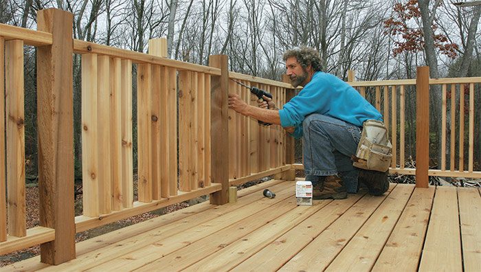 Fasten the top first. Spacer blocks hold the railing the correct height off the decking. A long extension helps to set the screws without the spinning driver marring the balusters.