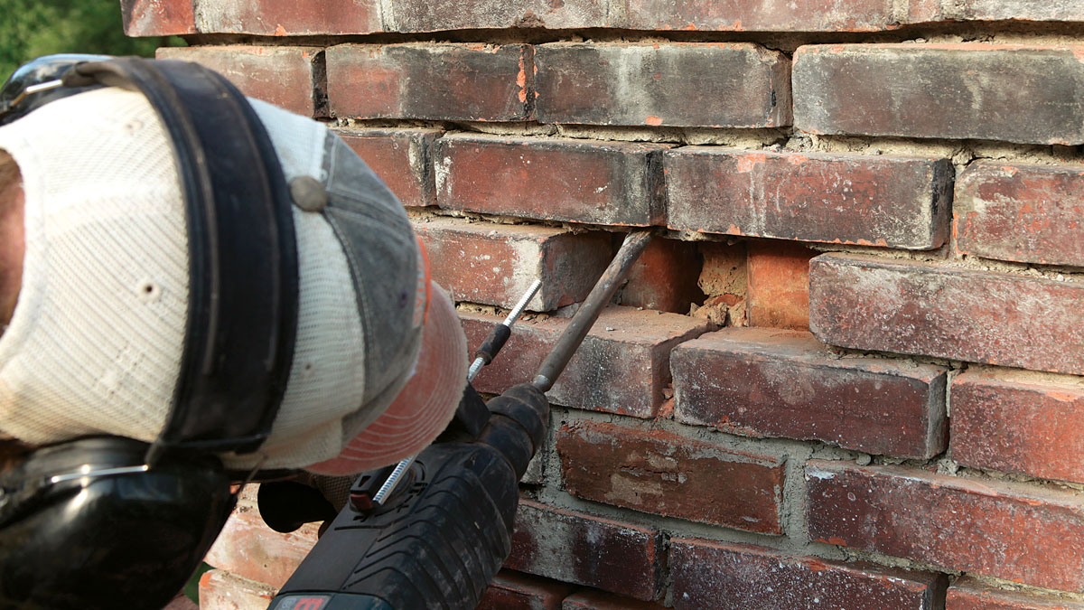 Soft power. Remove old mortar from bricks with a hammer drill and chisel set to hammer, angling as shallow as possible to the face of the brick. Barely pull the trigger. It often doesn’t take much for unconfined mortar to separate from the brick face.