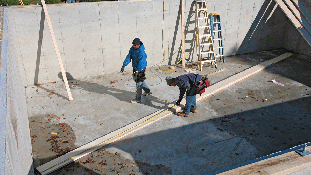 A poured concrete basement floor offers a perfect working surface for beam assembly. Double-check every layout measurement as the labeled pieces go together.