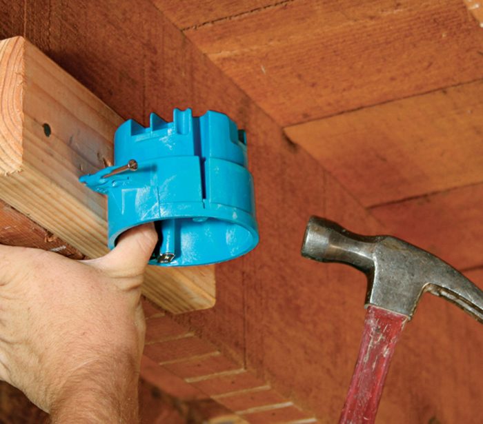 Man using a hammer to nail a box to a piece of blocking in order to offset its positon from a joist.