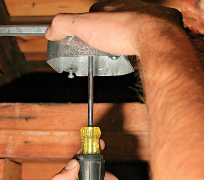 Man using a screwdriver to attach a metal box to an adjustable hanger.