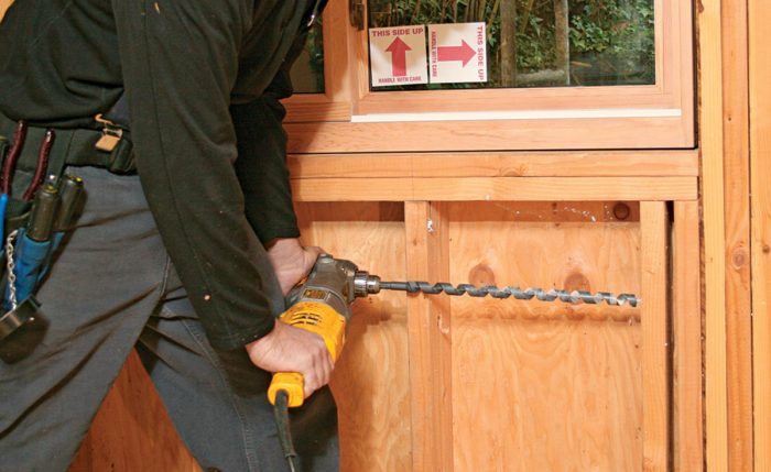 Man using a power drill with an 18 inch bit to go through multiple studs.