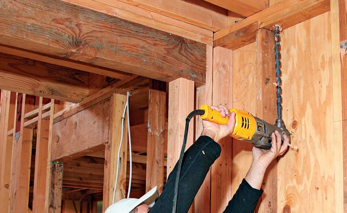 Man using a power drill with 18 inch bit to drill through top wall plates.