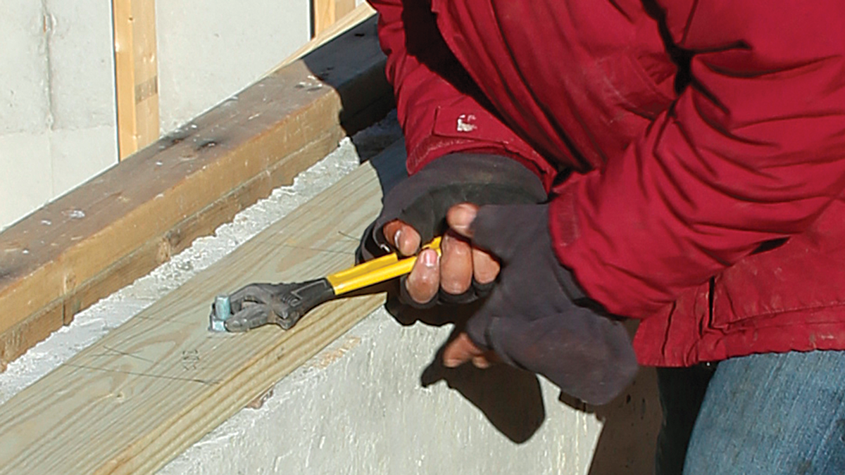 Tighten the anchor bolts. We put down a layer of foam sill gasket and transfer the anchor-bolt locations to the mudsill. Then we drill 5⁄8-in. holes to accommodate the bolts, which are capped with nuts and flat washers. We tighten the anchor bolts with an adjustable wrench until the wood fibers begin to compress.