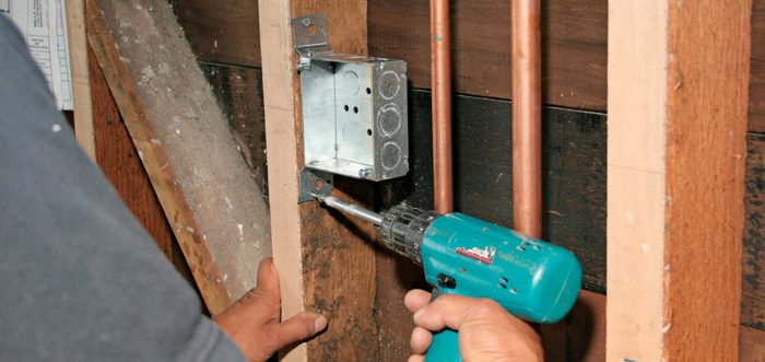 Man using a screw gun to attach a box with integral brackets to a stud.