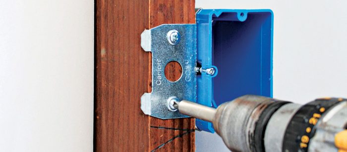 Using a screw gun to attach an adjustable box to a stud.