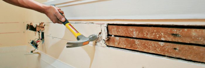 Using a hammer on a plaster wall to expose wiring