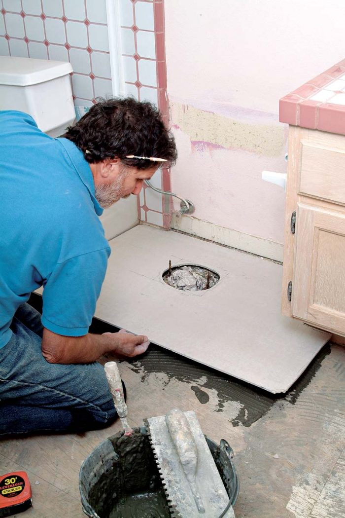 Lower the backerboard into place over the toilet flange, working its corner under the cabinet.