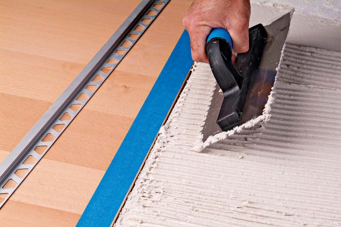 To install a trim strip between tile and an adjacent floor, comb thinset for the last row of tile.