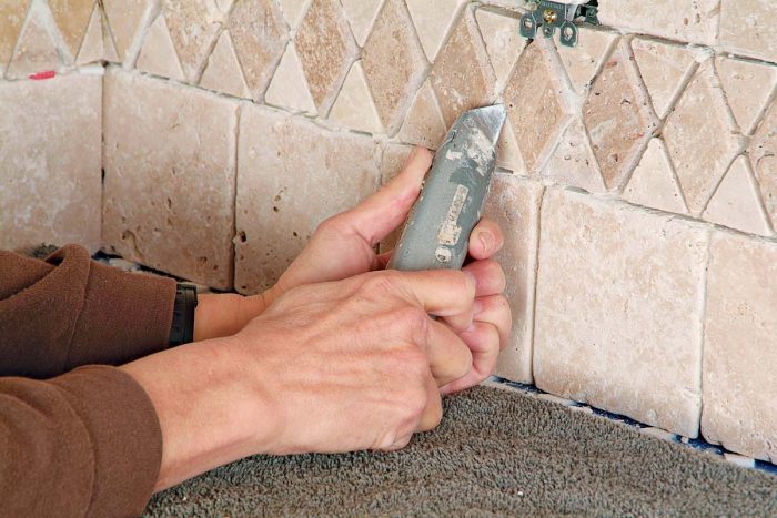 Use both hands to steady the utility knife as you scrape thinset from between grout lines. A slip can scratch stone tiles.