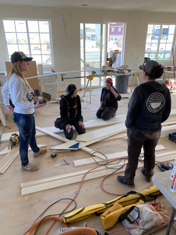 A group of women in work gear collaborating around wood planks and tools