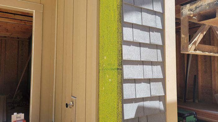 A patch of yellow mesh rainscreen visible from behind siding