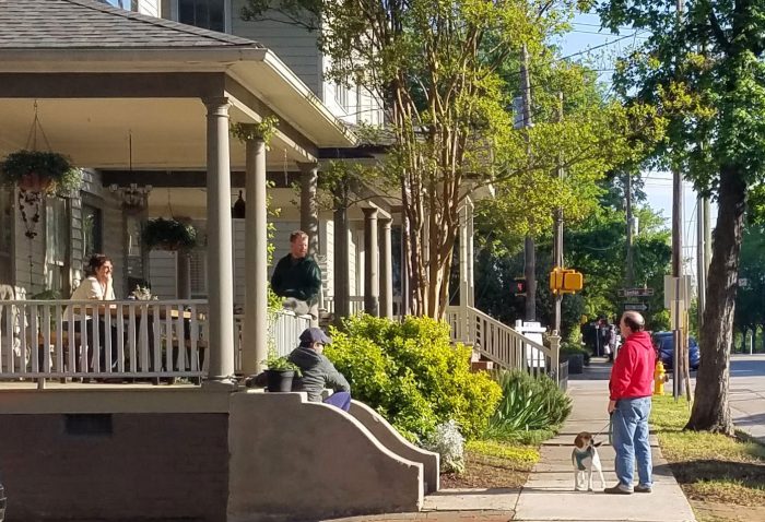 People sitting on porch talking to people on a sidewalk