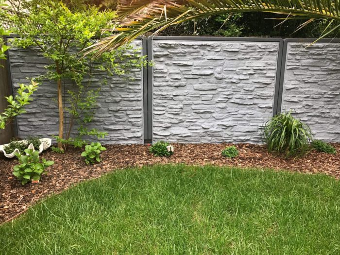 Image of a stone fence panels in a backyard surrounded by grass and plants