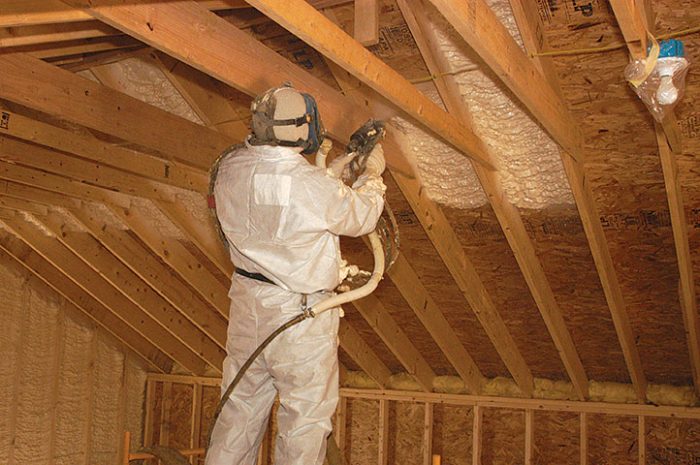 A person in safety gear spraying in foam in an attic