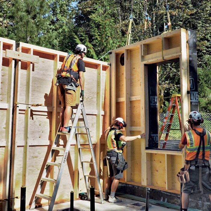 A crew of three placing wall panels on the foundation of a panelized house