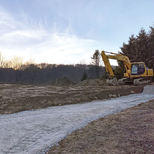 Photo of a gravel driveway with an earth mover on the righthand side.