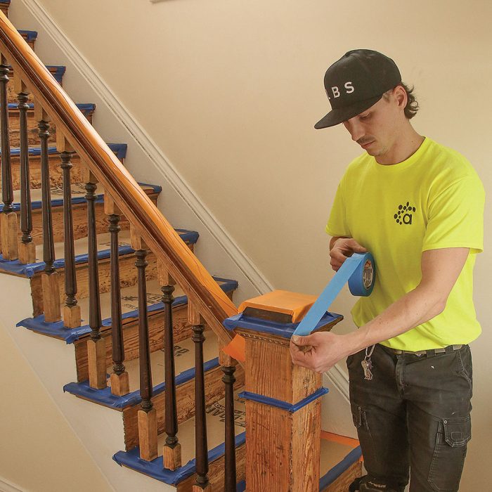 Photo of a man in a neon yellow shirt putting masking tape on stairs.