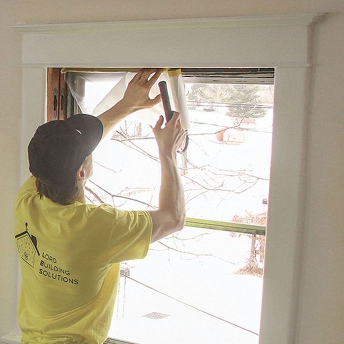 Photo of a man in a neon yellow shirt putting tape over storm sash.