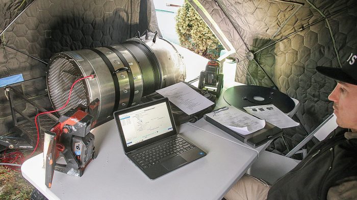 Photo of a man monitoring the sealing process on a computer in a tent outside the house.