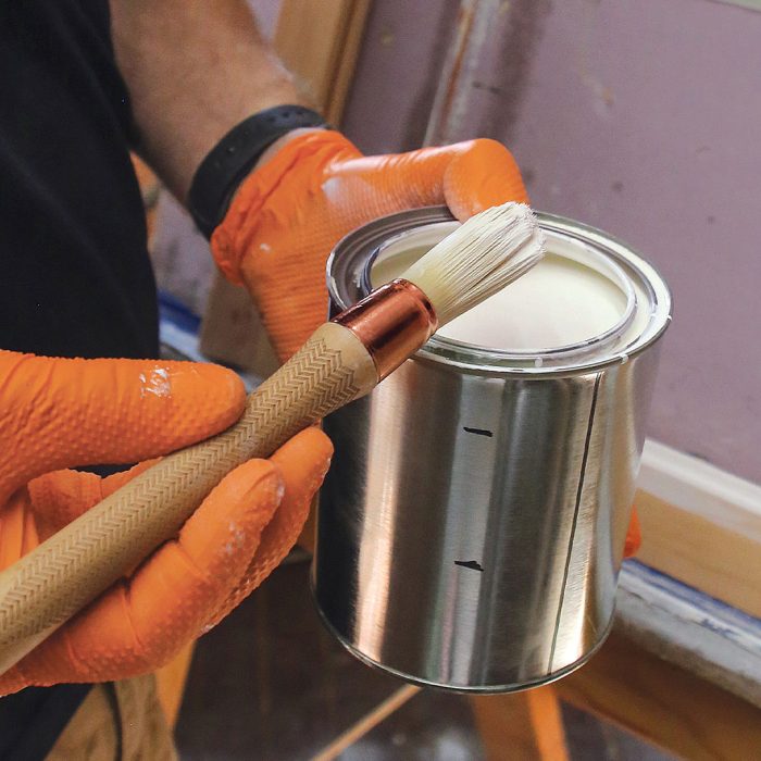 Photo of a hand holding a paint can with linseed oil in it and a paint brush.