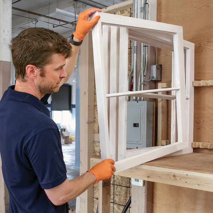 Photo of a man wearing orange gloves putting a painted window frame in a drying rack.