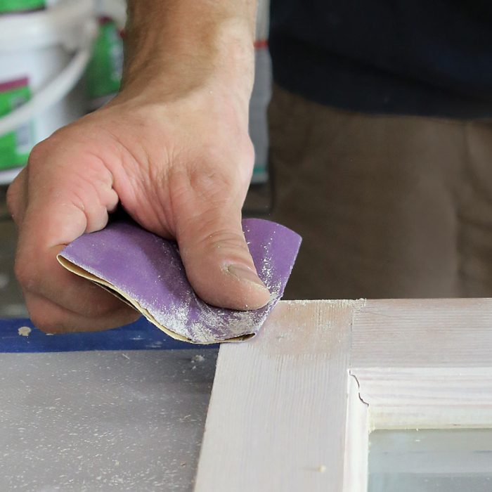 Photo of a hand sanding the corner of a window frame after the first coat of linseed oil paint.