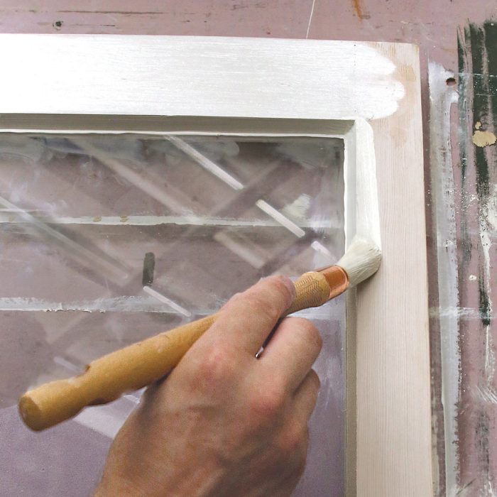 Photo of a hand putting a second coat of linseed oil paint on a window frame.